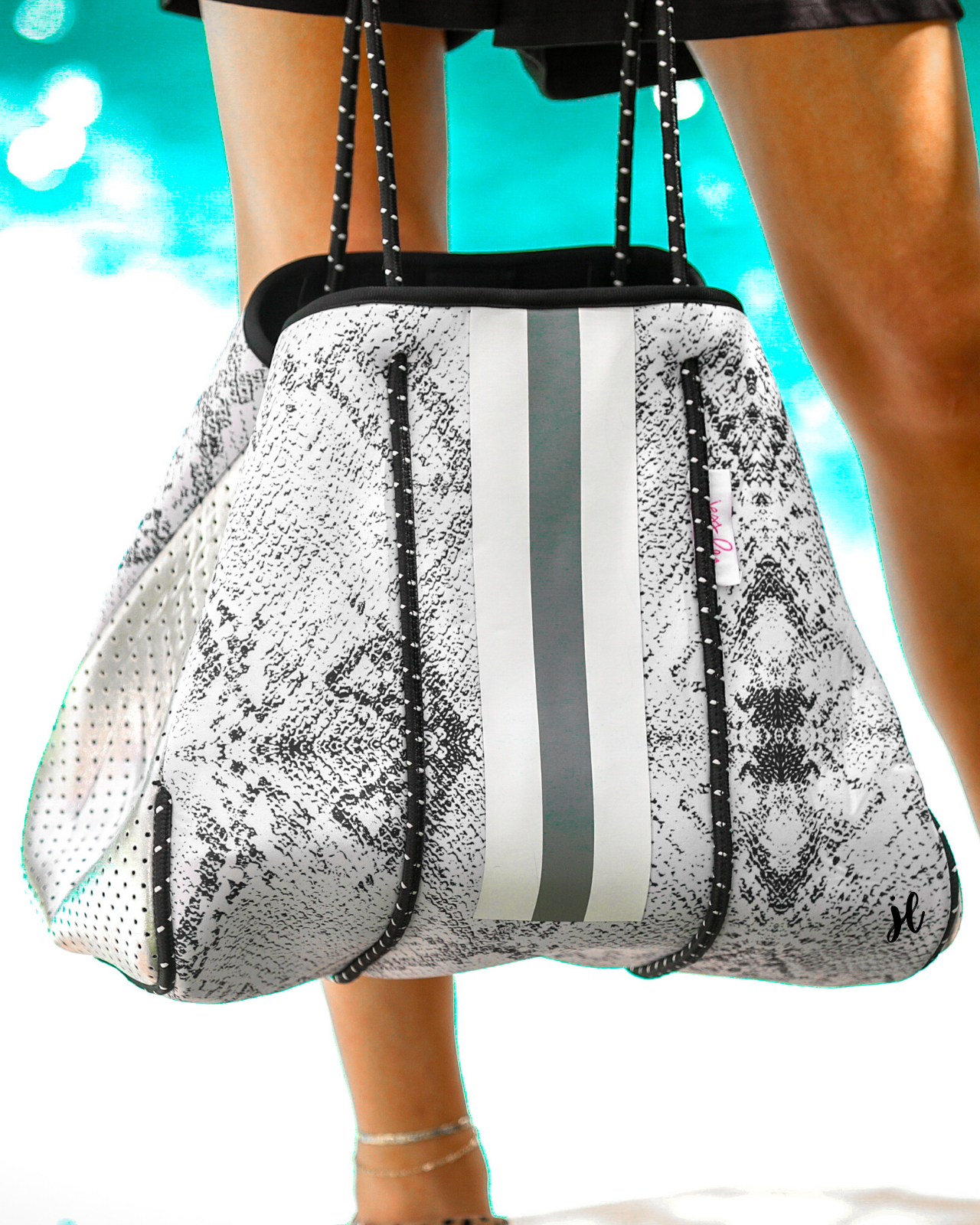 ultra-lightweight tote made of neoprene with a removable hard bottom liner, paracord shoulder straps, removable matching zippered pouch, magnetic side snap closures in silver hardware, black interior (tote and pouch), and racing stripes (gray and white)