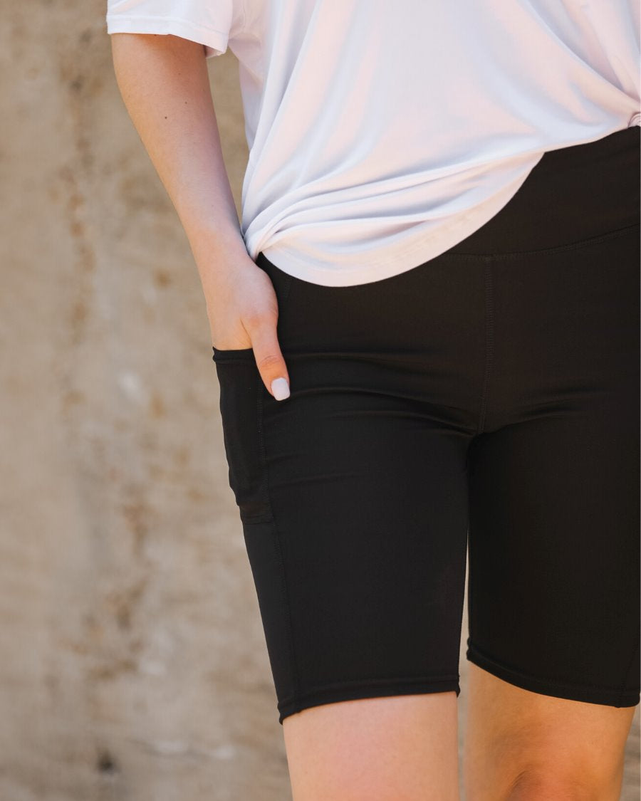sleek black biker shorts crafted from lightweight stretch fabric with a high elastic waistband for tummy control, side pockets, a flattering figure-hugging short silhouette, above-knee length, and pull-on design