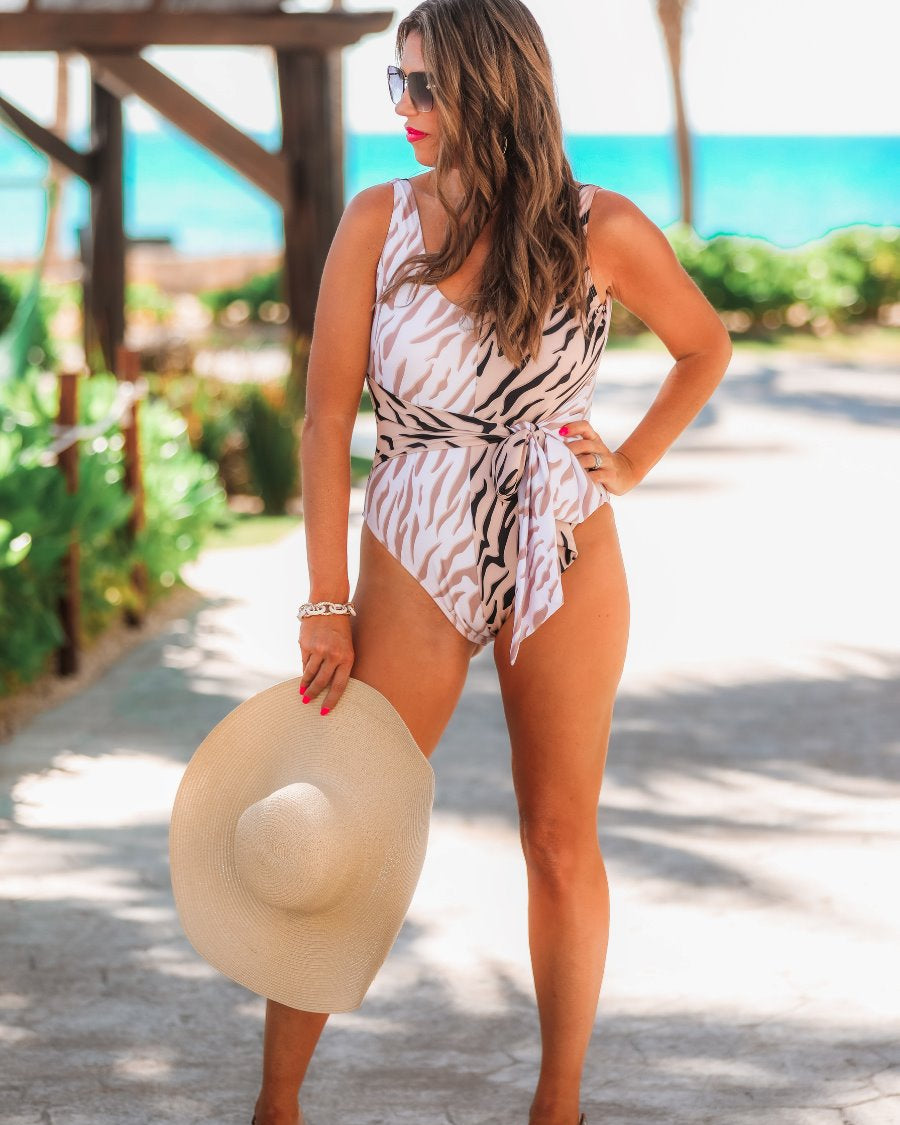 a one-piece swimsuit made of stretchy material with a scoop back, chunky straps, a versatile accent tie, and removable padding on a neutral color block animal print pattern fabric