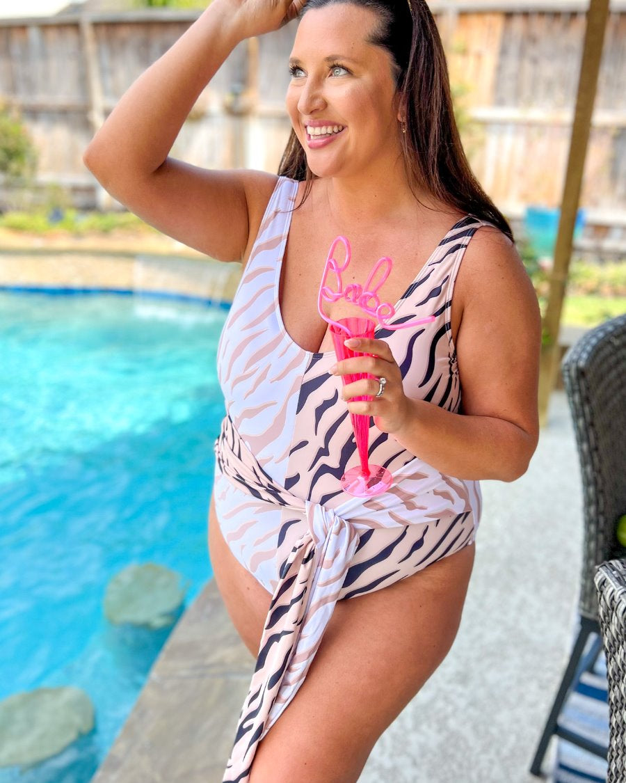 a one-piece swimsuit made of stretchy material with a scoop back, chunky straps, a versatile accent tie, and removable padding on a neutral color block animal print pattern fabric