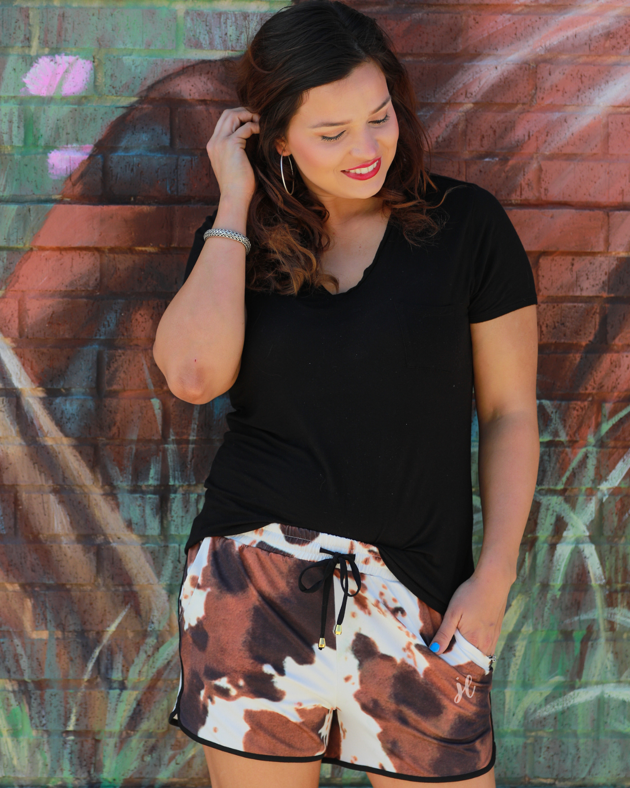 mid-rise relaxed fit activewear shorts with side pockets and a tie waist drawstring with gold bead accents, designed on a classic black, brown, and white cow patterned print fabric and black trim
