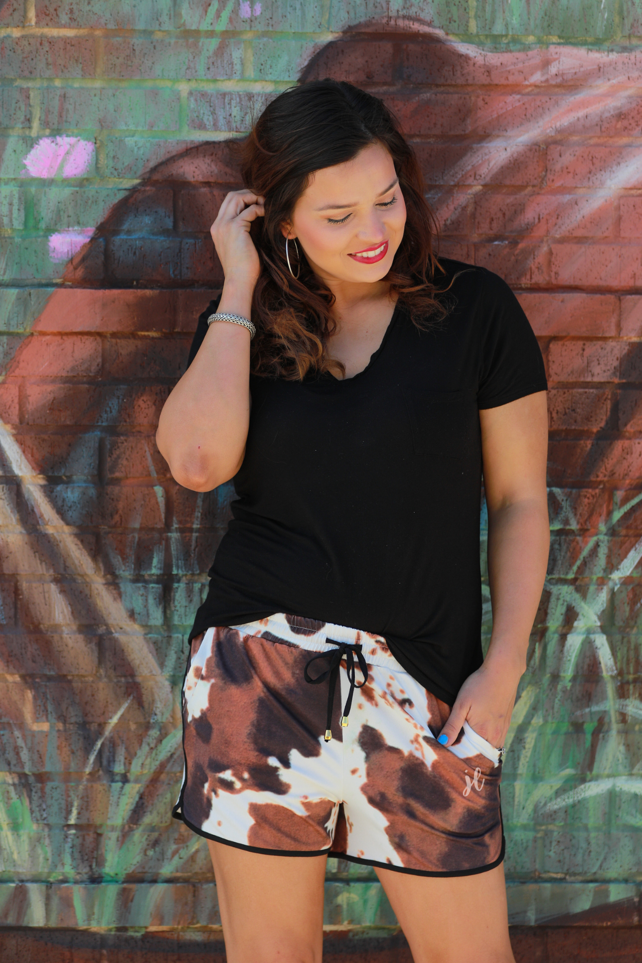 mid-rise relaxed fit activewear shorts with side pockets and a tie waist drawstring with gold bead accents, designed on a classic black, brown, and white cow patterned print fabric and black trim