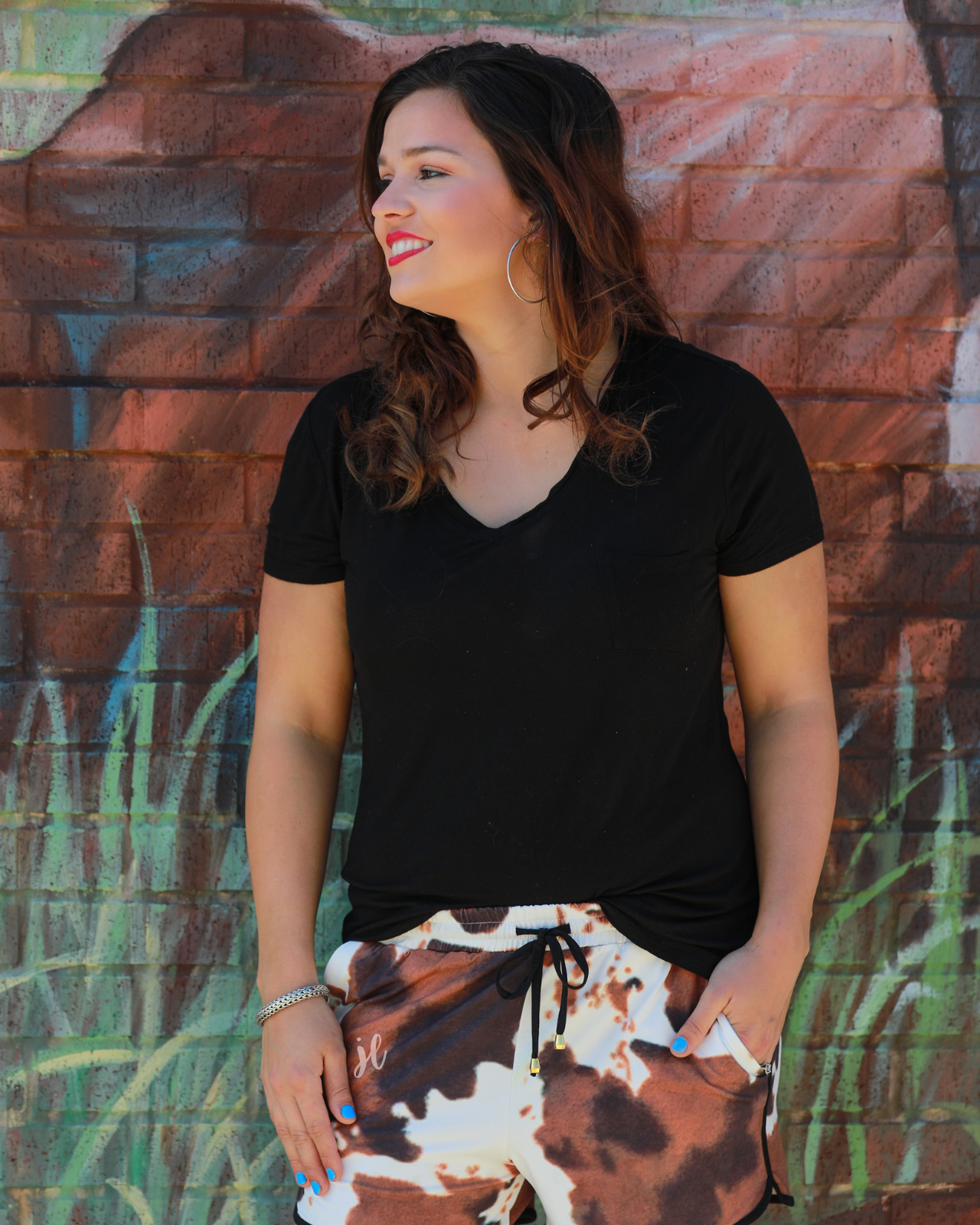mid-rise relaxed fit activewear shorts with side pockets and a tie waist drawstring with gold bead accents, designed on a classic black, brown, and white cow patterned print fabric and black trim