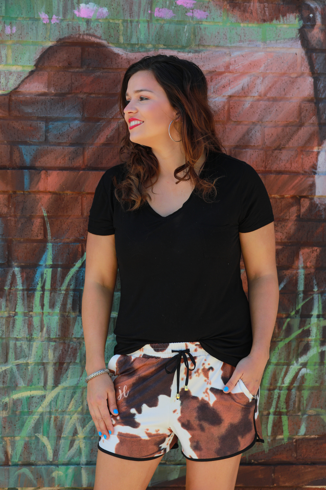 mid-rise relaxed fit activewear shorts with side pockets and a tie waist drawstring with gold bead accents, designed on a classic black, brown, and white cow patterned print fabric and black trim