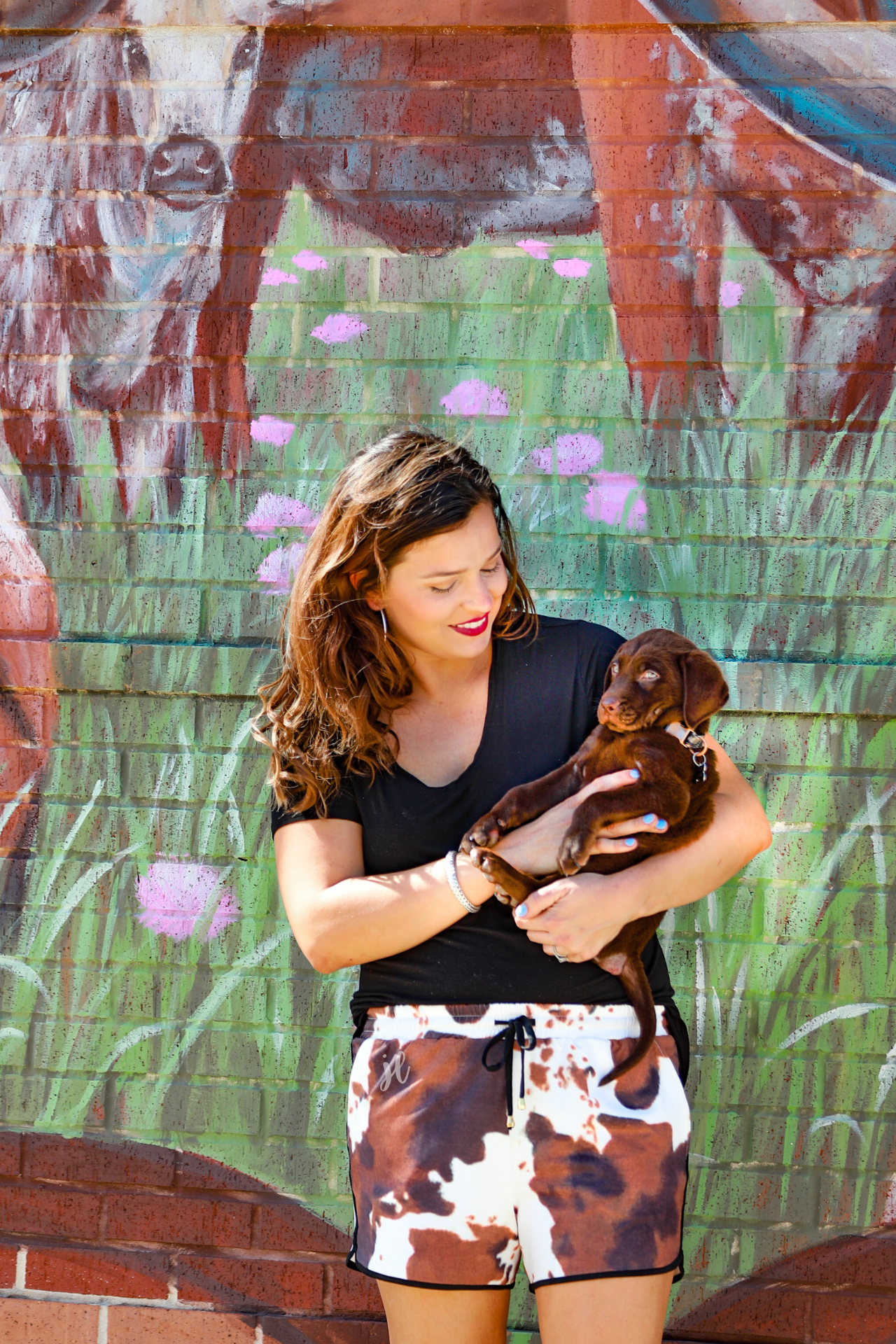 mid-rise relaxed fit activewear shorts with side pockets and a tie waist drawstring with gold bead accents, designed on a classic black, brown, and white cow patterned print fabric and black trim