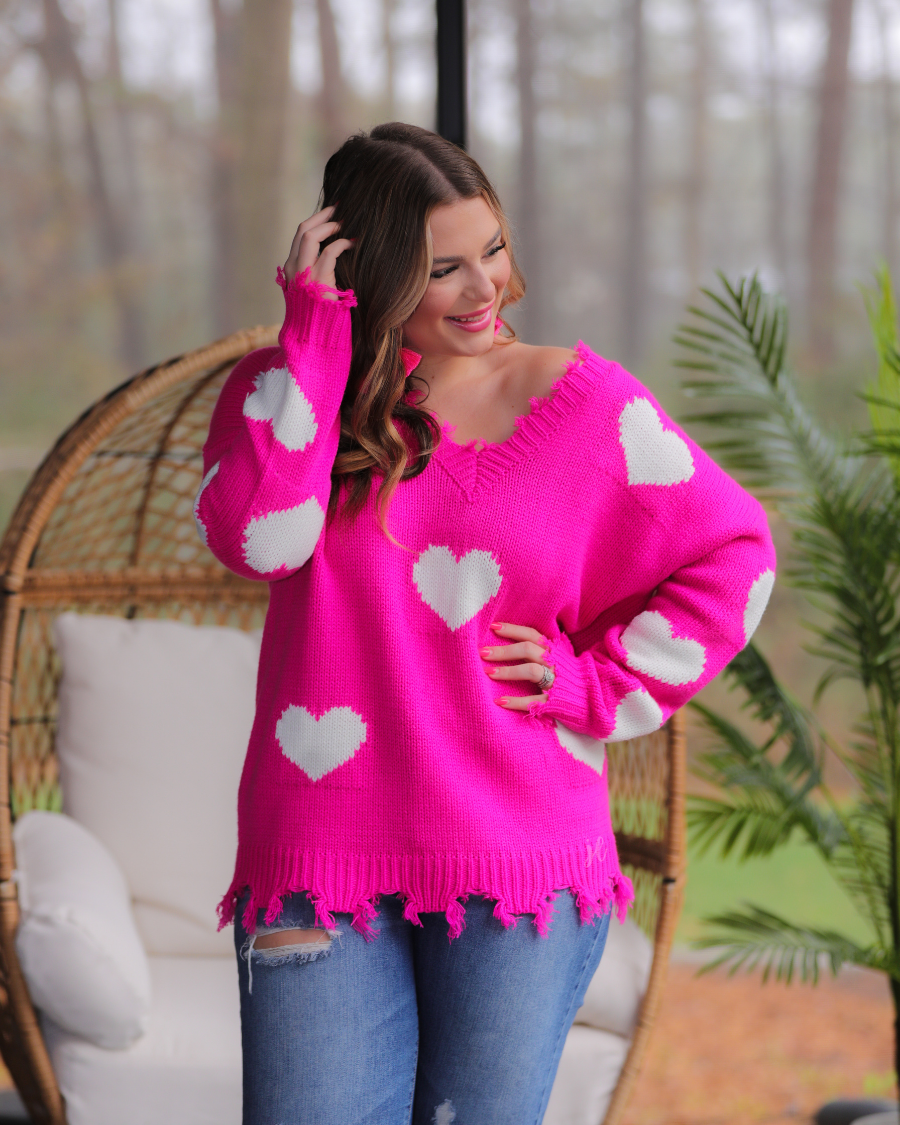 an oversized distressed v-neck long-sleeve sweater with a white heart pattern on a pink knit fabric