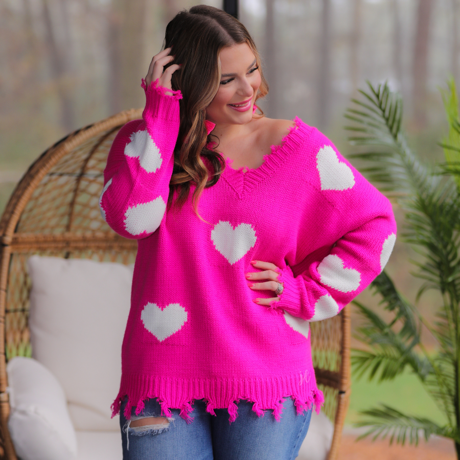 an oversized distressed v-neck long-sleeve sweater with a white heart pattern on a pink knit fabric
