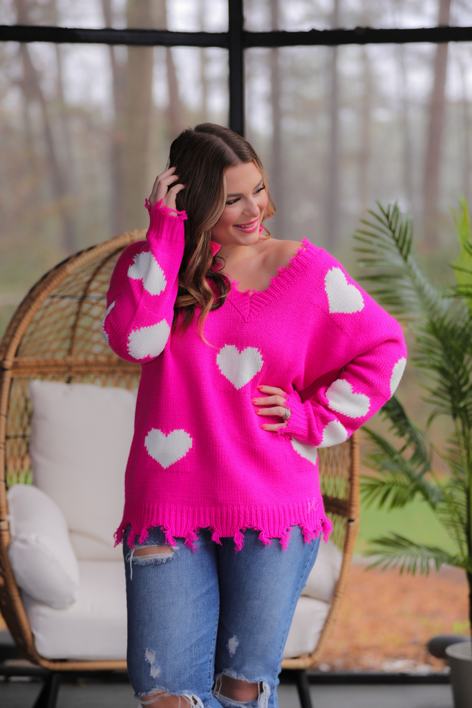 an oversized distressed v-neck long-sleeve sweater with a white heart pattern on a pink knit fabric 