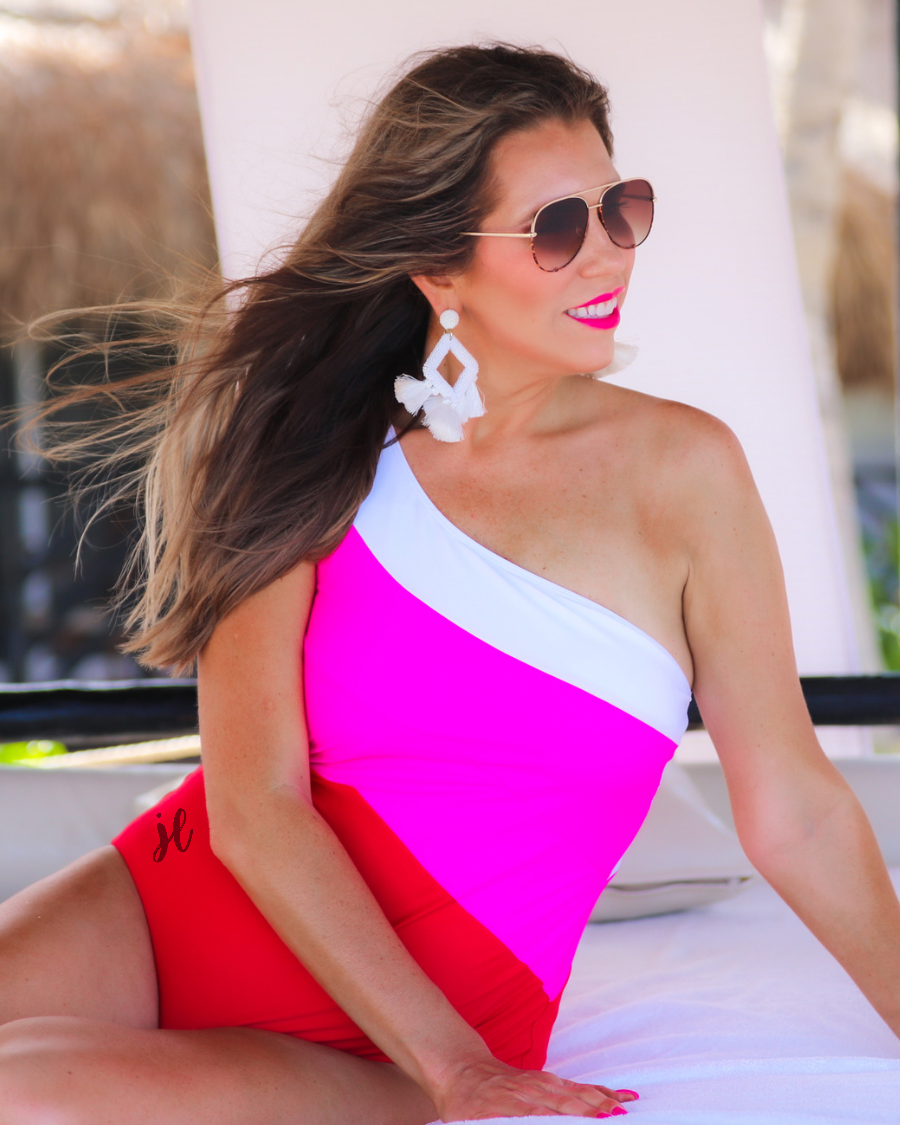 one-piece swimsuit made of stretchy material with a white, pink, and red slanted color block style, a chunky one-shoulder strap, and removable padding