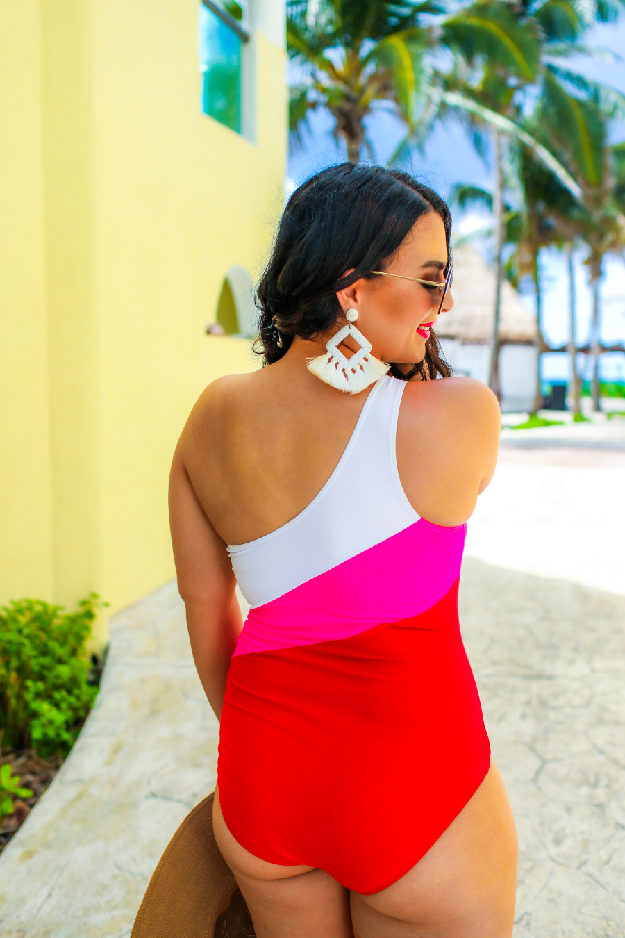 one-piece swimsuit made of stretchy material with a white, pink, and red slanted color block style, a chunky one-shoulder strap, and removable padding