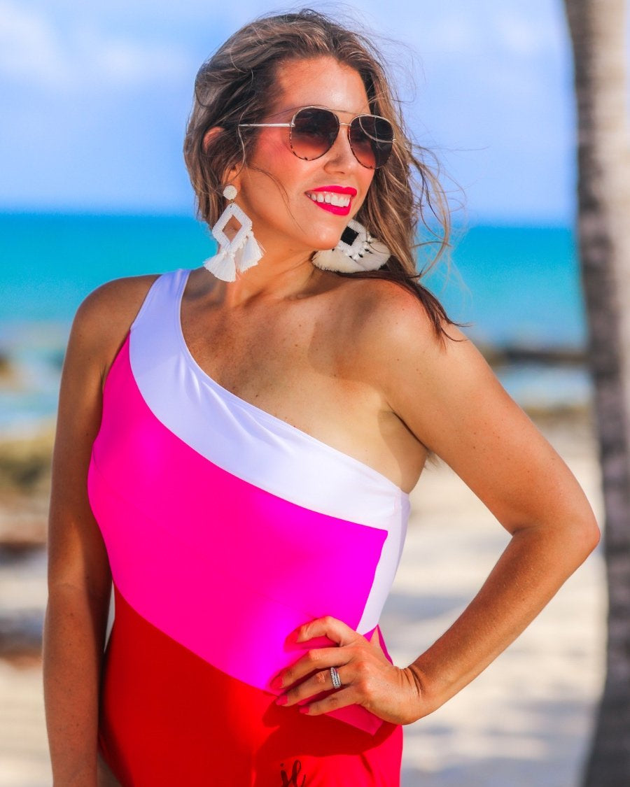 one-piece swimsuit made of stretchy material with a white, pink, and red slanted color block style, a chunky one-shoulder strap, and removable padding