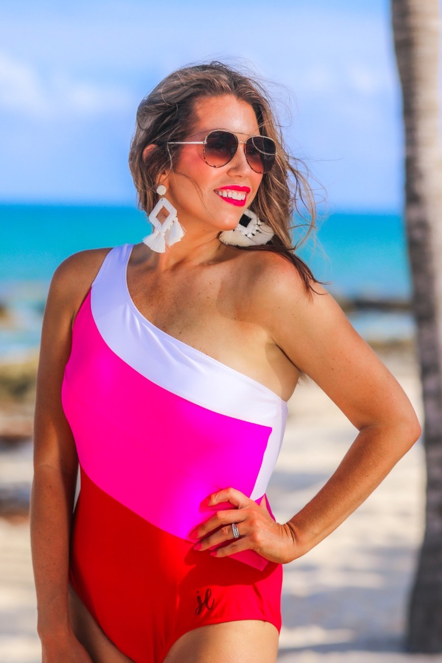 one-piece swimsuit made of stretchy material with a white, pink, and red slanted color block style, a chunky one-shoulder strap, and removable padding