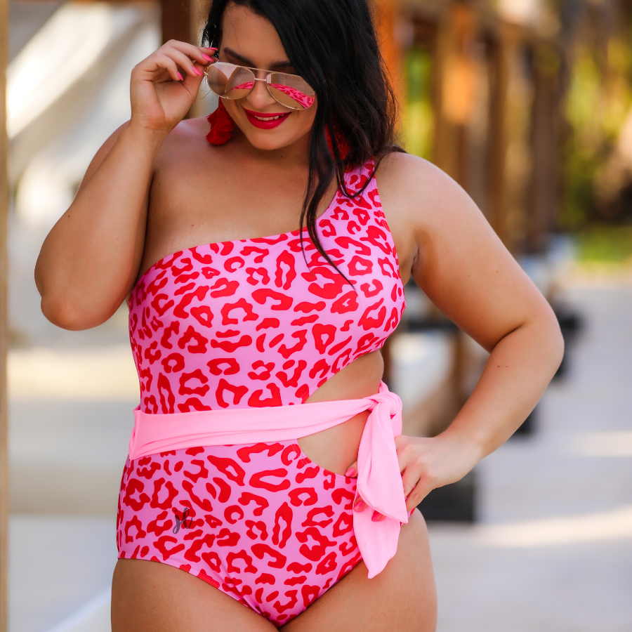 one-shoulder swimsuit made of stretchy material with a side cutout, a wrap-around tie, and removable padding on a two-toned pink leopard print fabric