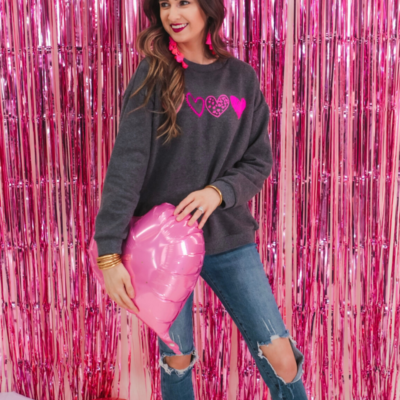 a charcoal long-sleeve sweatshirt with a fuzzy inside, sewn-on pink chenille heart patches, a relaxed drop-shoulder fit, and ribbed detailing on the classic crew neckline, cuffs, and hemline