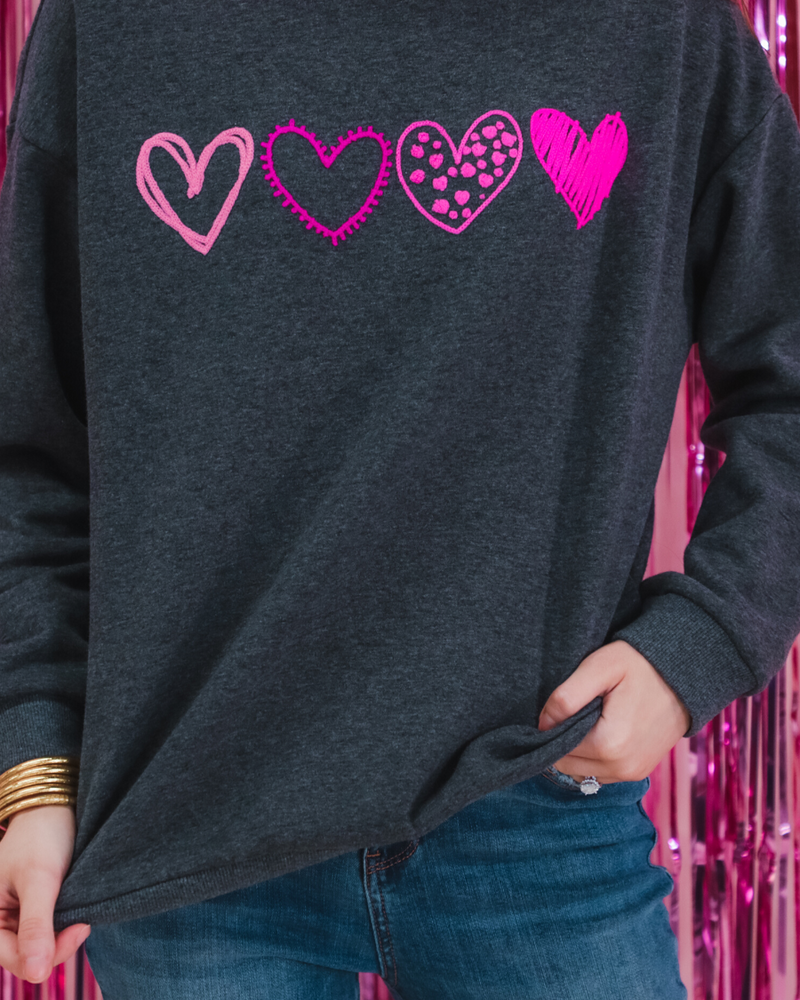 a charcoal long-sleeve sweatshirt with a fuzzy inside, sewn-on pink chenille heart patches, a relaxed drop-shoulder fit, and ribbed detailing on the classic crew neckline, cuffs, and hemline