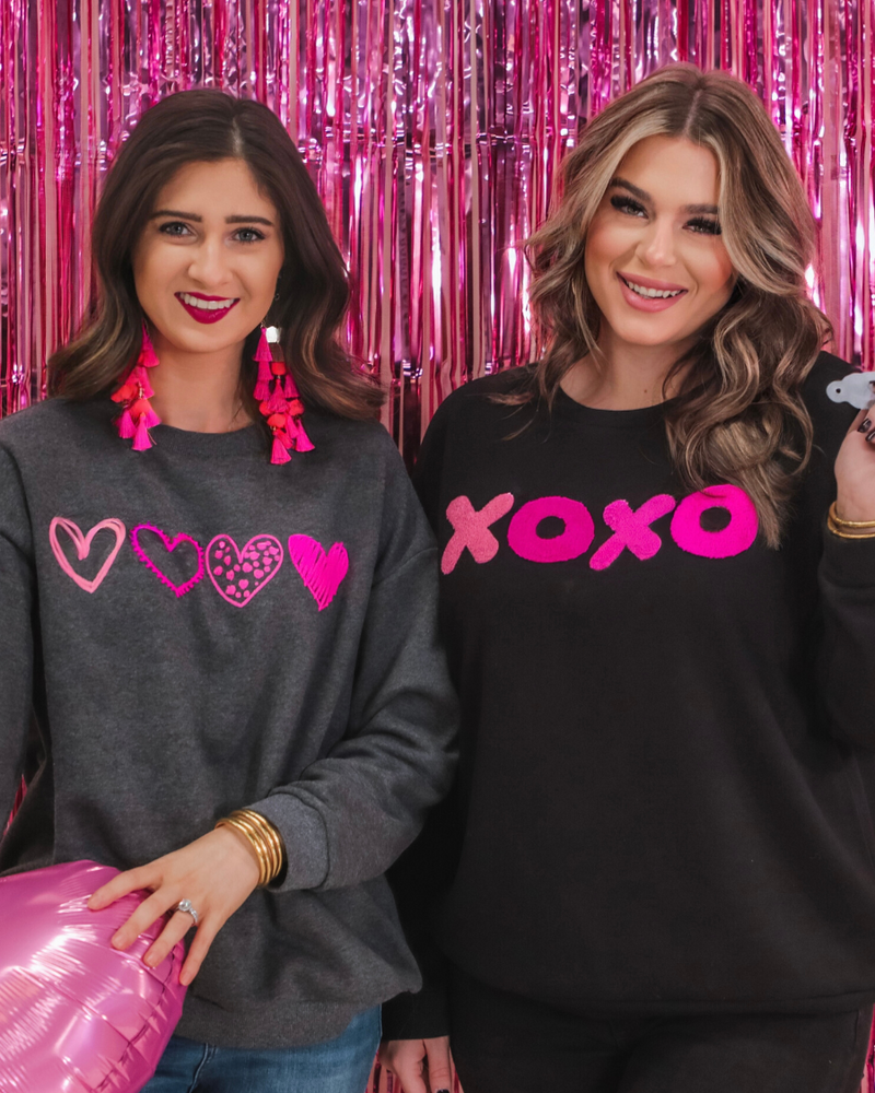 a charcoal long-sleeve sweatshirt with a fuzzy inside, sewn-on pink chenille heart patches, a relaxed drop-shoulder fit, and ribbed detailing on the classic crew neckline, cuffs, and hemline
