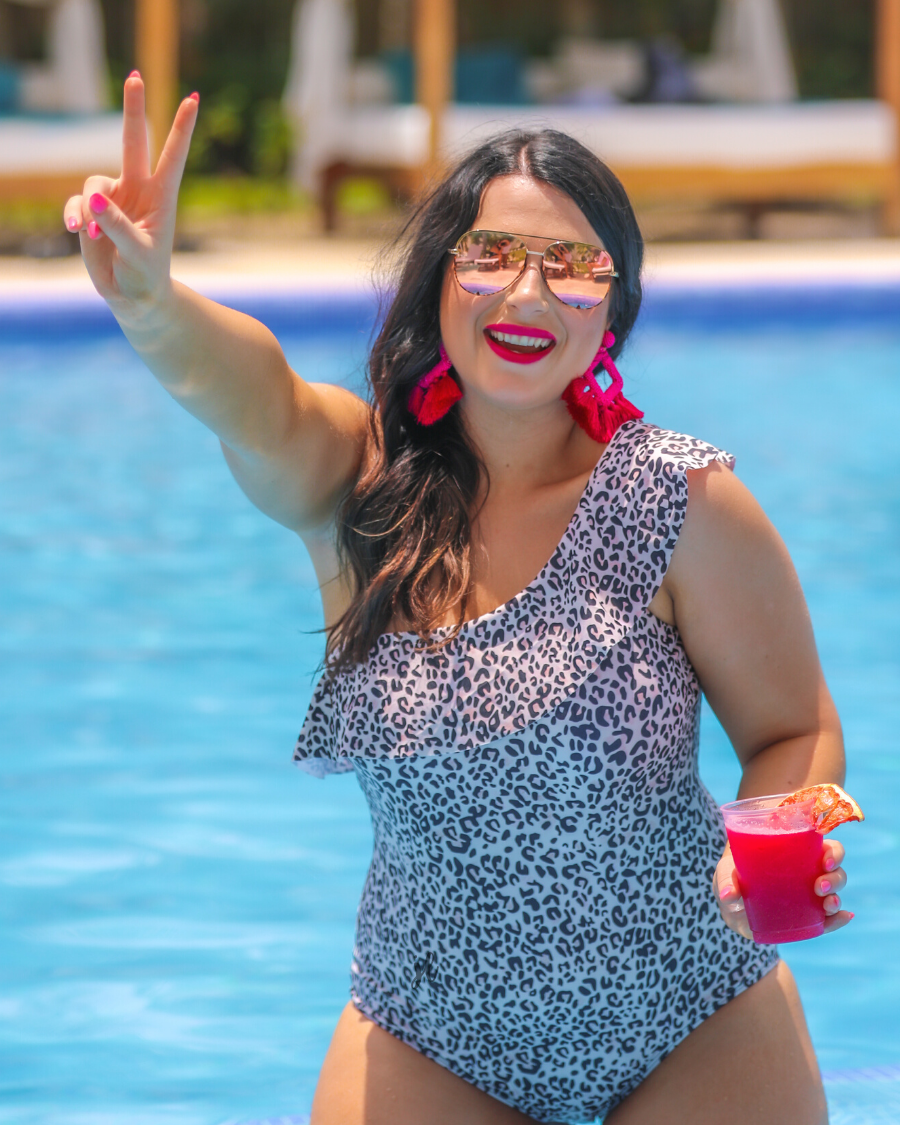 a one-piece swimsuit made from stretchy swim fabric with a black and neutral leopard print, one-shoulder ruffled neckline, and removable padding