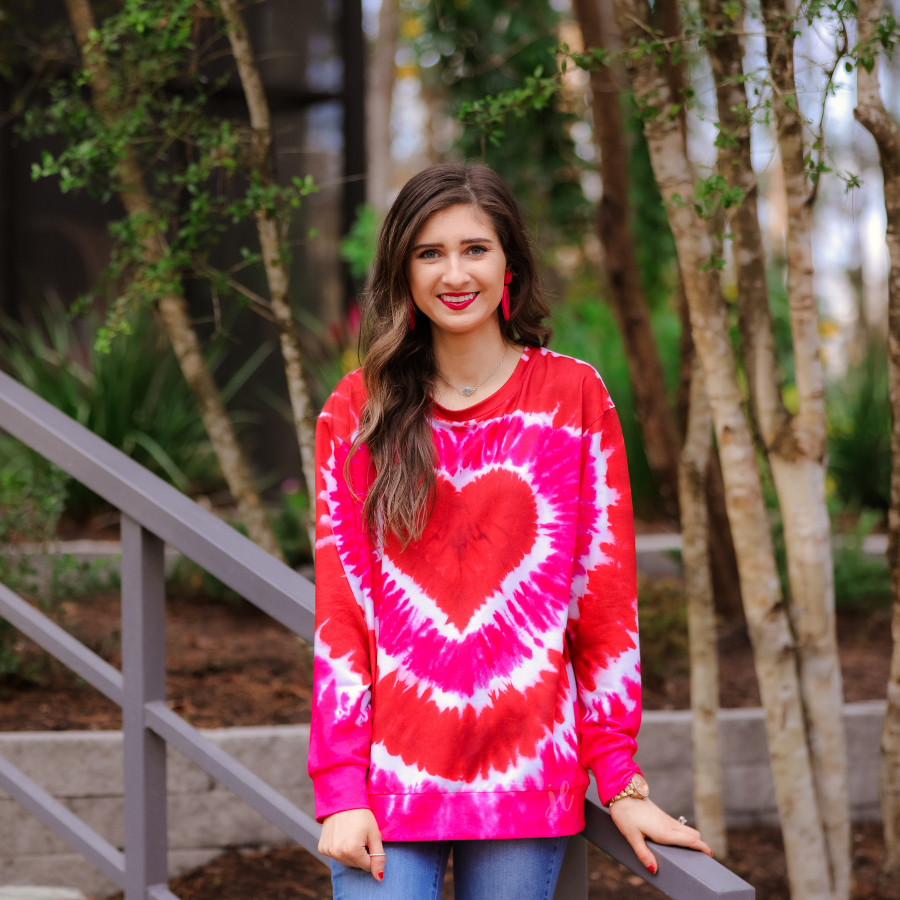 a red lightweight long-sleeve knit top with a bold heart motif layered over a vibrant tie-dye pattern, a flattering scoop neckline, and a streamlined silhouette that finished with a straight hem