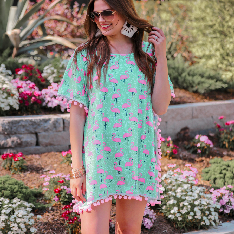 lightweight coverup made of breezy material with playful light pink pom pom decorative trim and fun pink flamingo print on a mint background