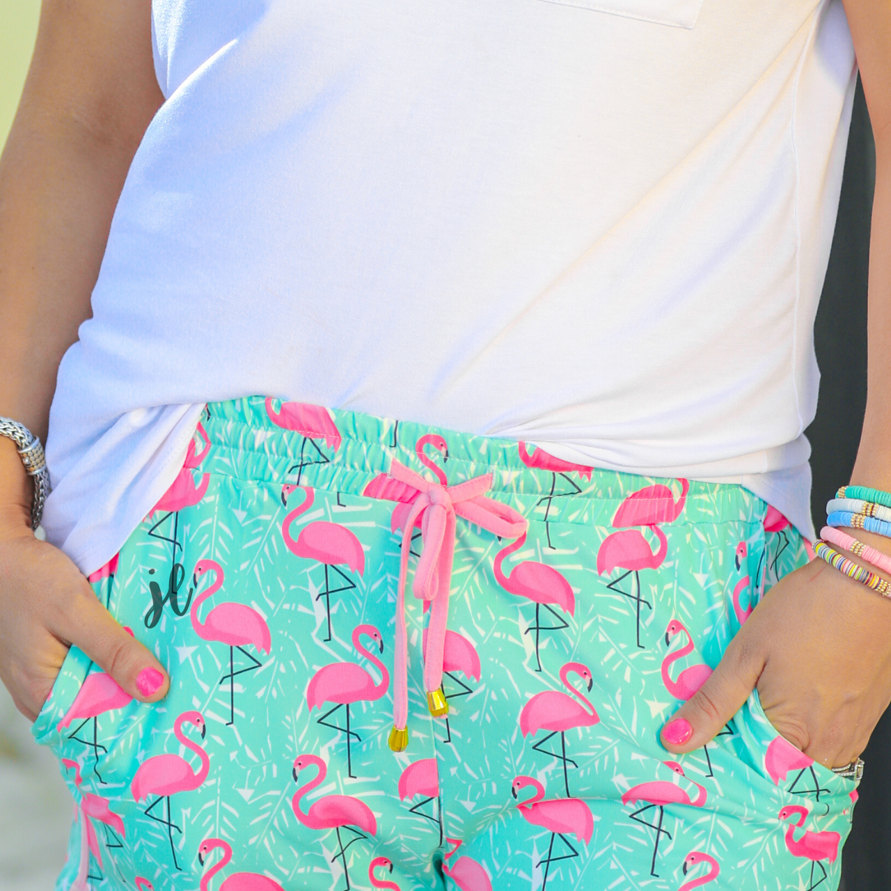 mid-rise relaxed fit activewear shorts with side pockets and a tie waist drawstring with gold bead accents, designed on a hot pink flamingo and white palm leaf pattern print fabric, mint base, and pink trim