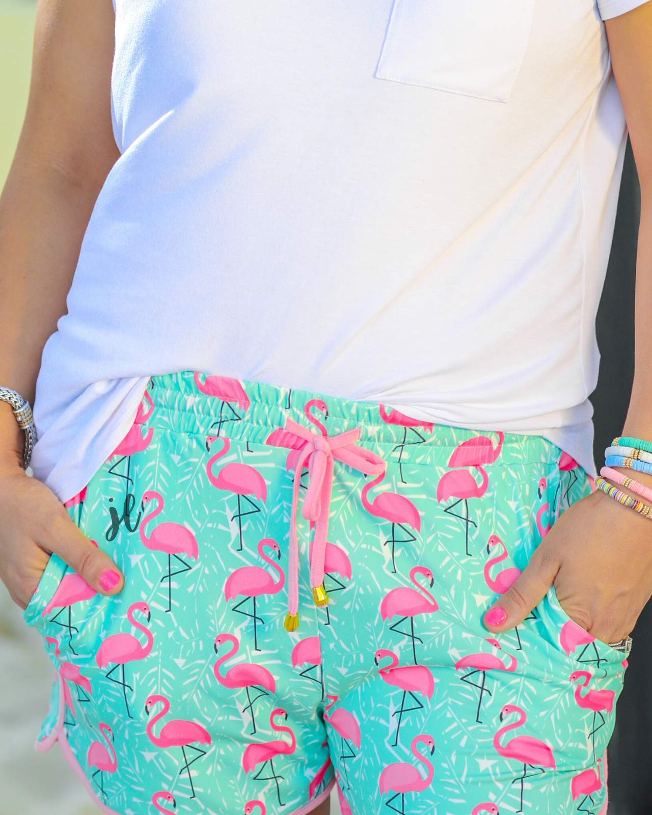 mid-rise relaxed fit activewear shorts with side pockets and a tie waist drawstring with gold bead accents, designed on a hot pink flamingo and white palm leaf pattern print fabric, mint base, and pink trim