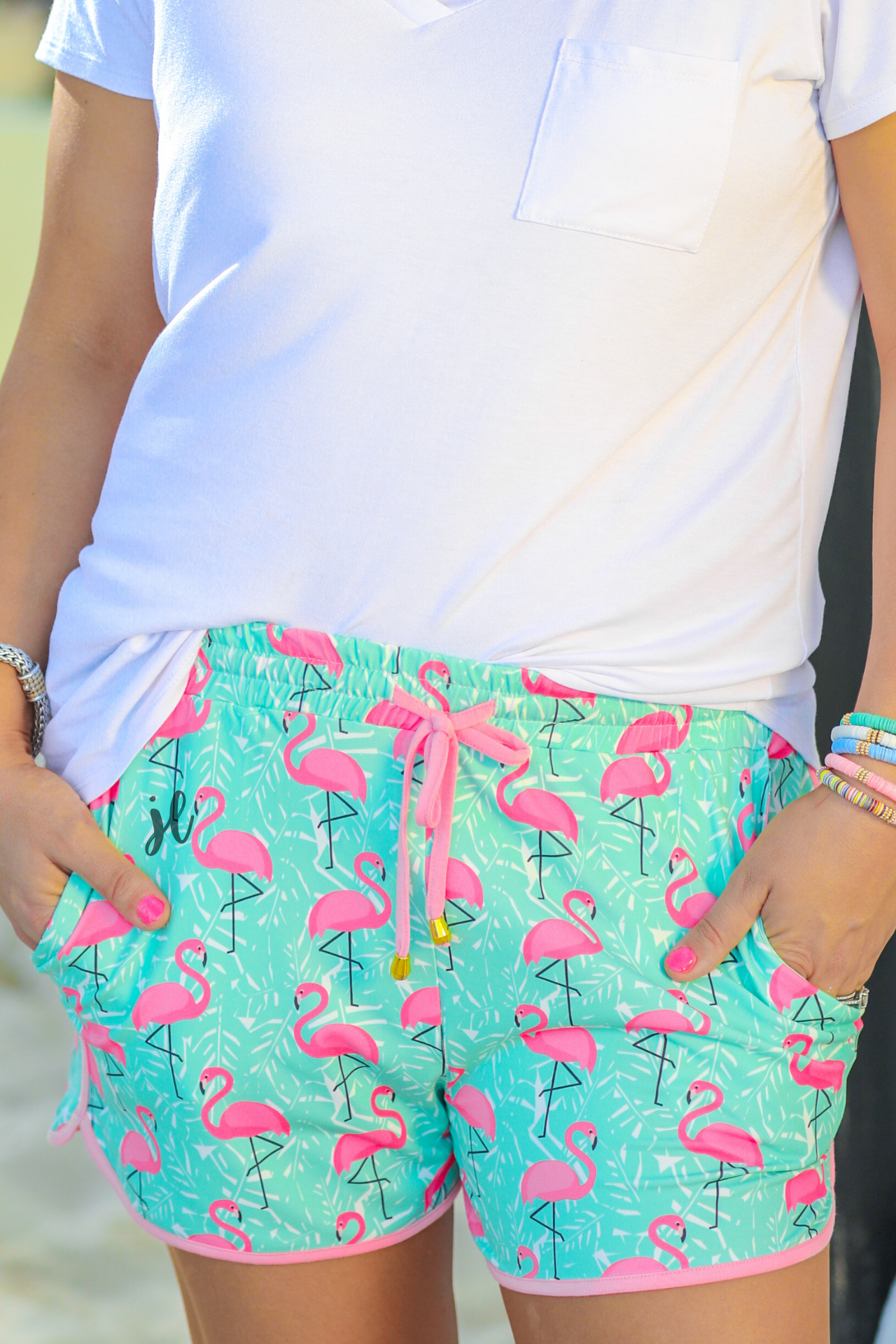 mid-rise relaxed fit activewear shorts with side pockets and a tie waist drawstring with gold bead accents, designed on a hot pink flamingo and white palm leaf pattern print fabric, mint base, and pink trim
