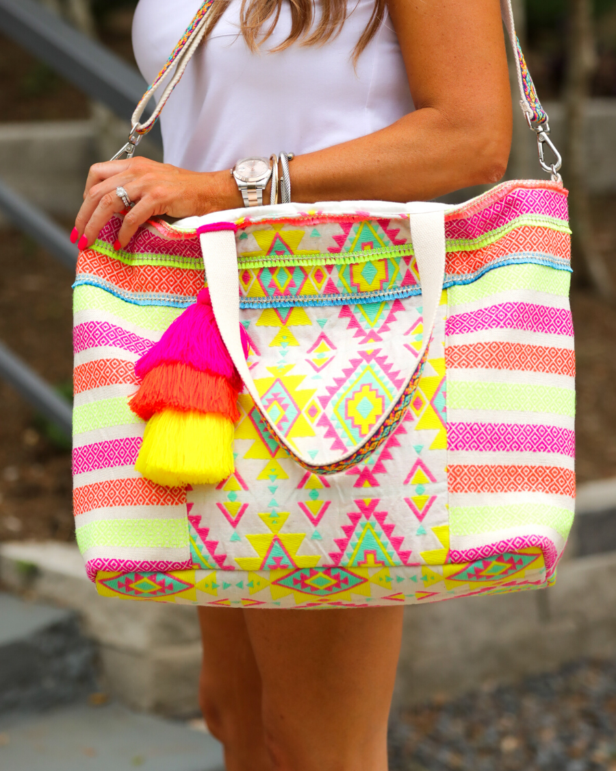 double-handle canvas bag with a removable three-tier neon tassel (pink, orange, and yellow), full-zipper closure, a removable adjustable strap (bohemian trim ribbon braid), and interior pockets (two open, one zip) on a geometric and stripe multicolor pattern print