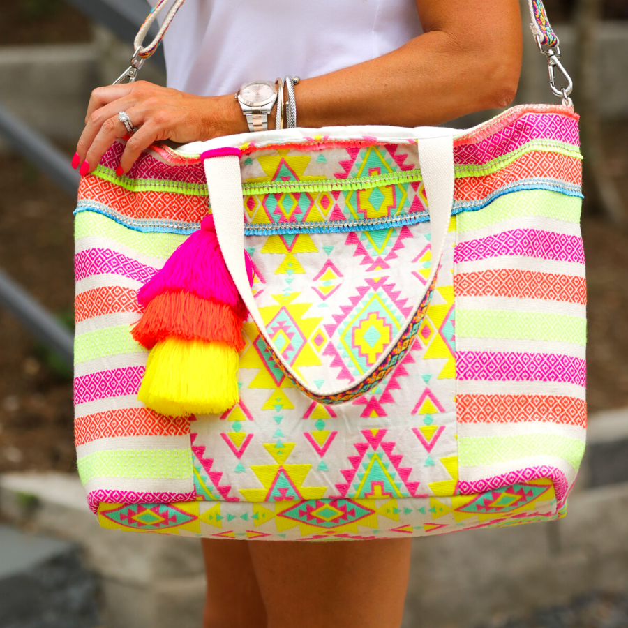 double-handle canvas bag with a removable three-tier neon tassel (pink, orange, and yellow), full-zipper closure, a removable adjustable strap (bohemian trim ribbon braid), and interior pockets (two open, one zip) on a geometric and stripe multicolor pattern print