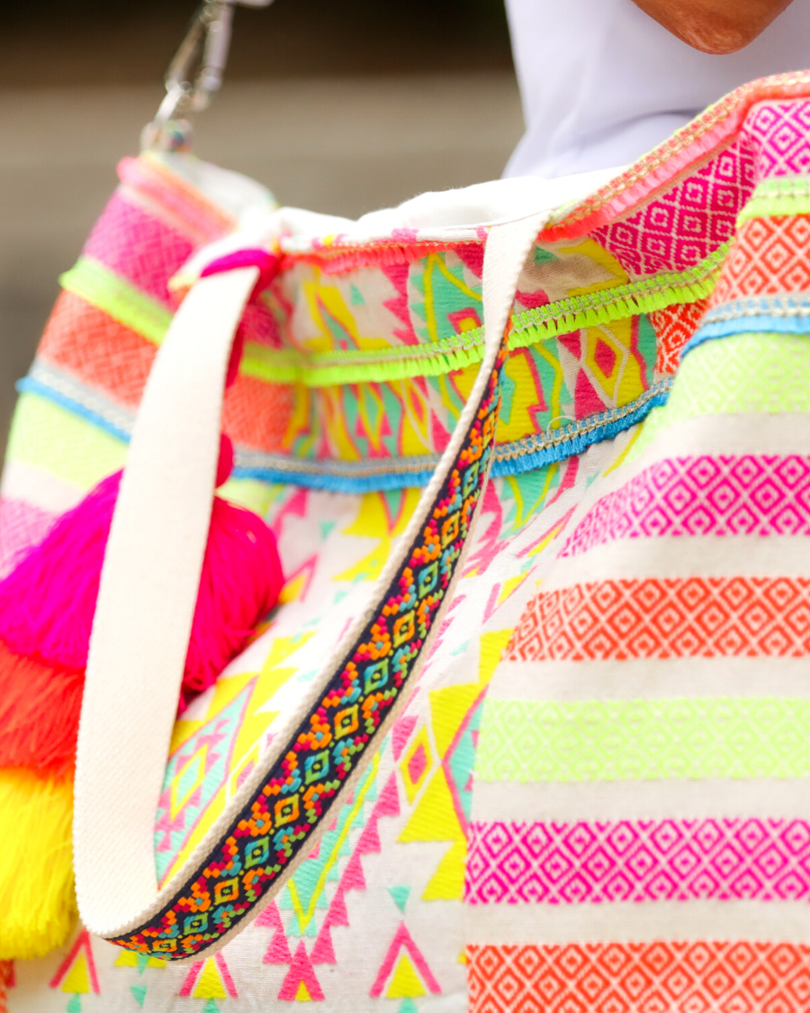 double-handle canvas bag with a removable three-tier neon tassel (pink, orange, and yellow), full-zipper closure, a removable adjustable strap (bohemian trim ribbon braid), and interior pockets (two open, one zip) on a geometric and stripe multicolor pattern print