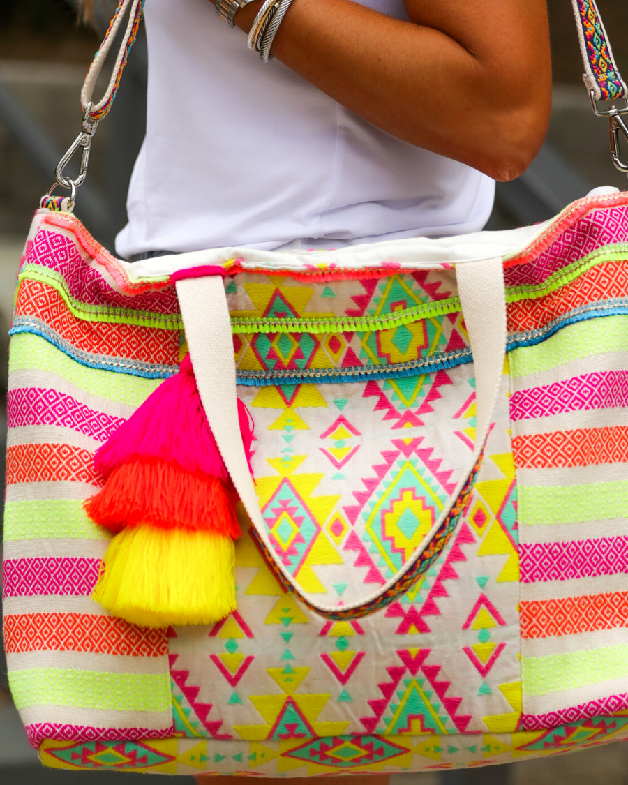 double-handle canvas bag with a removable three-tier neon tassel (pink, orange, and yellow), full-zipper closure, a removable adjustable strap (bohemian trim ribbon braid), and interior pockets (two open, one zip) on a geometric and stripe multicolor pattern print
