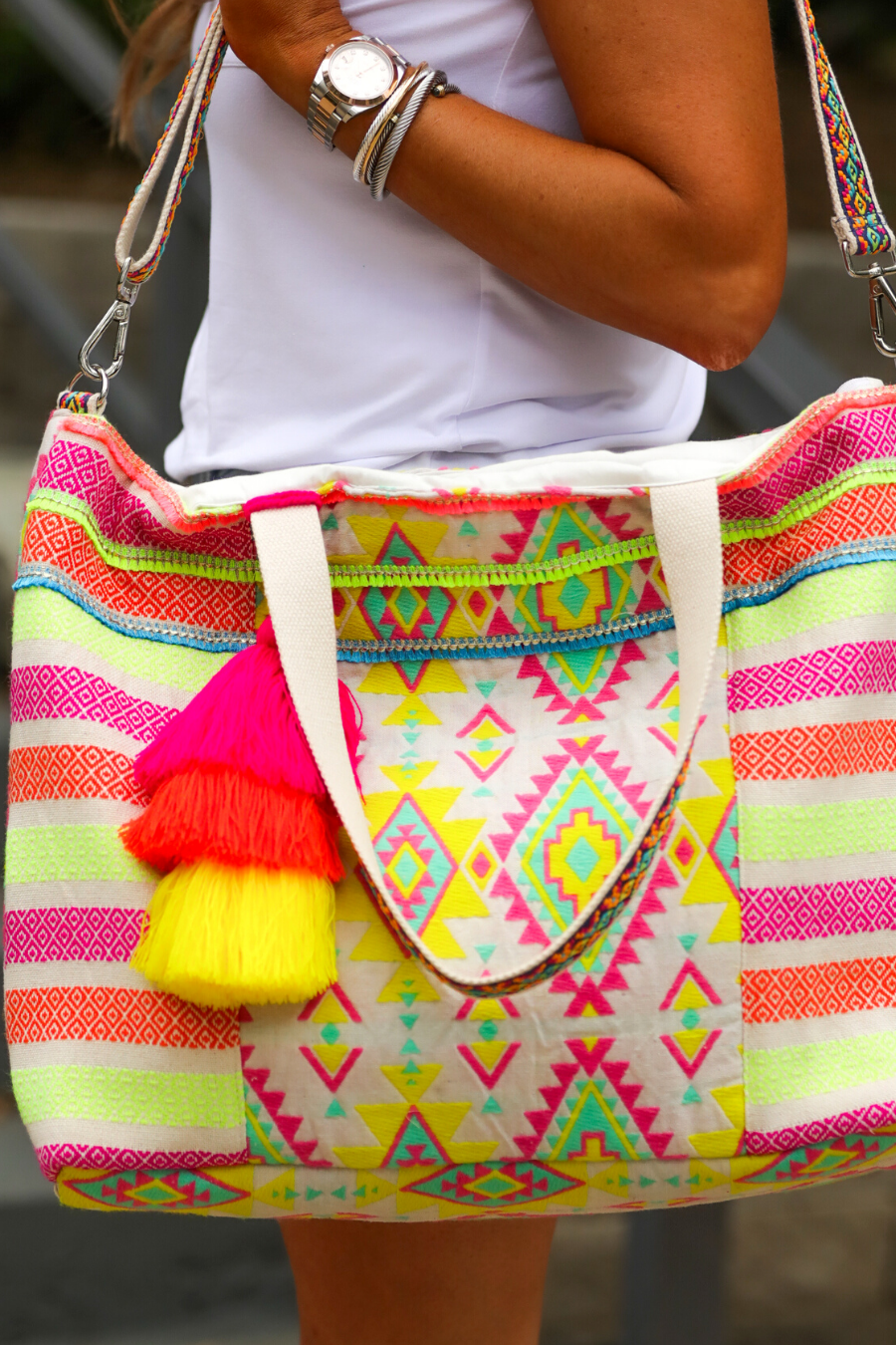 double-handle canvas bag with a removable three-tier neon tassel (pink, orange, and yellow), full-zipper closure, a removable adjustable strap (bohemian trim ribbon braid), and interior pockets (two open, one zip) on a geometric and stripe multicolor pattern print