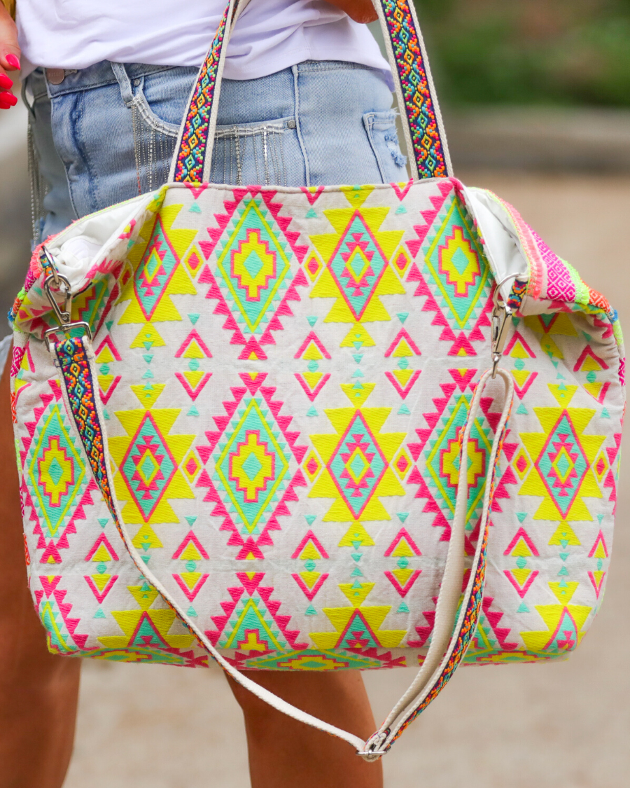 double-handle canvas bag with a removable three-tier neon tassel (pink, orange, and yellow), full-zipper closure, a removable adjustable strap (bohemian trim ribbon braid), and interior pockets (two open, one zip) on a geometric and stripe multicolor pattern print