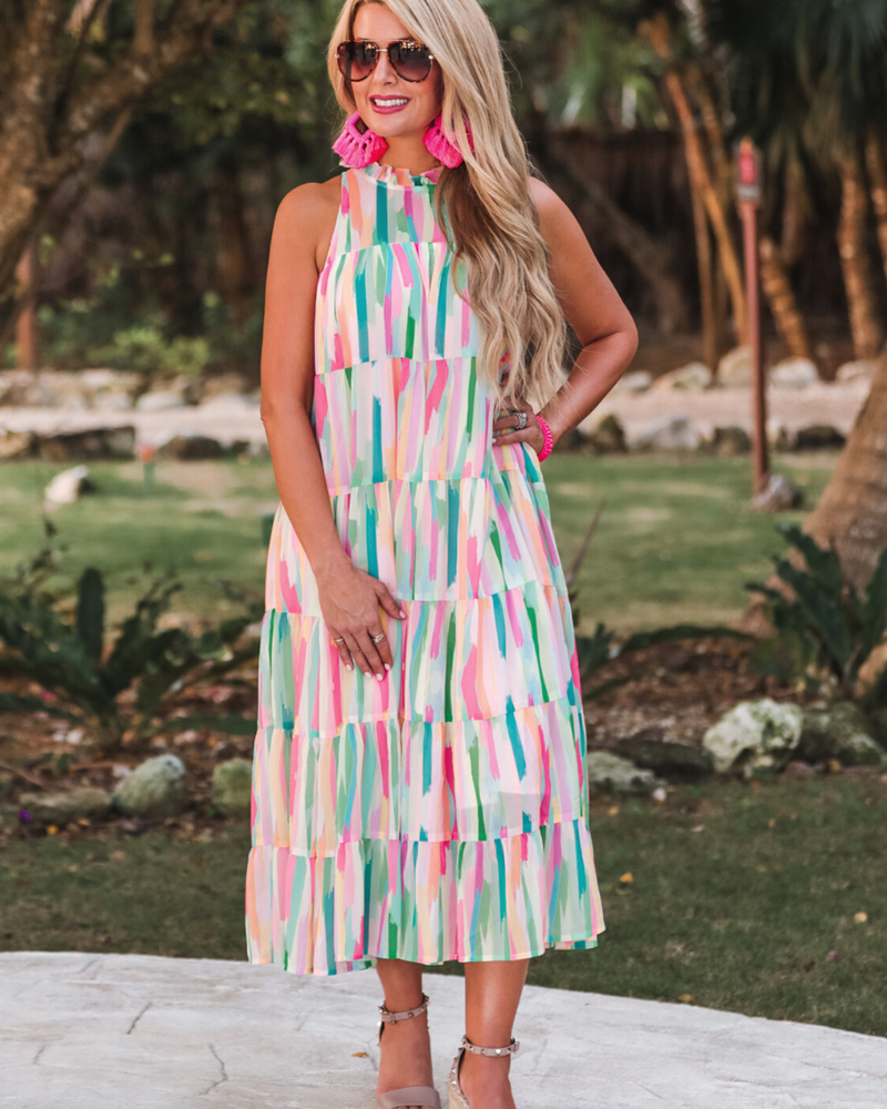 sleeveless dress with a ruffled halter neckline, singular button closure, tiered babydoll style silhouette, and a midi length with lining on a painterly print fabric in multi