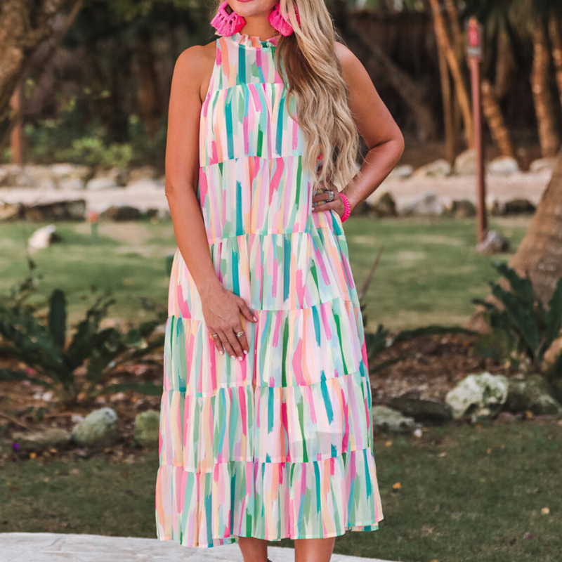 sleeveless dress with a ruffled halter neckline, singular button closure, tiered babydoll style silhouette, and a midi length with lining on a painterly print fabric in multi