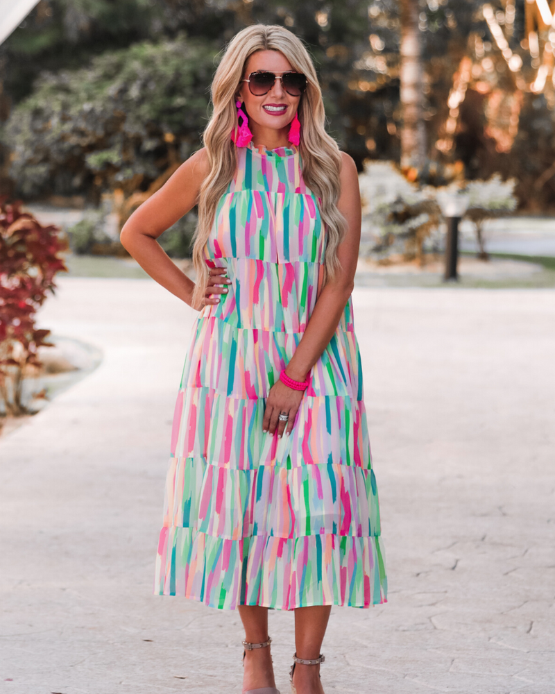 sleeveless dress with a ruffled halter neckline, singular button closure, tiered babydoll style silhouette, and a midi length with lining on a painterly print fabric in multi