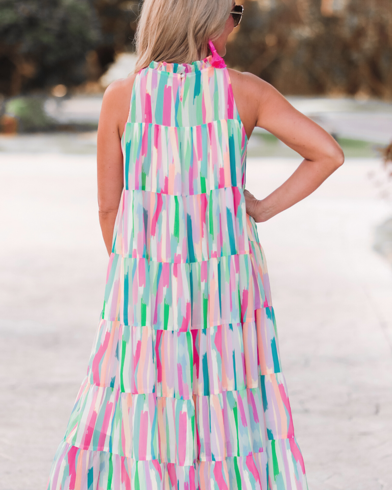 sleeveless dress with a ruffled halter neckline, singular button closure, tiered babydoll style silhouette, and a midi length with lining on a painterly print fabric in multi