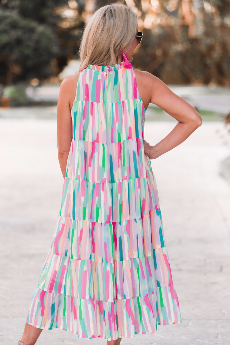 sleeveless dress with a ruffled halter neckline, singular button closure, tiered babydoll style silhouette, and a midi length with lining on a painterly print fabric in multi