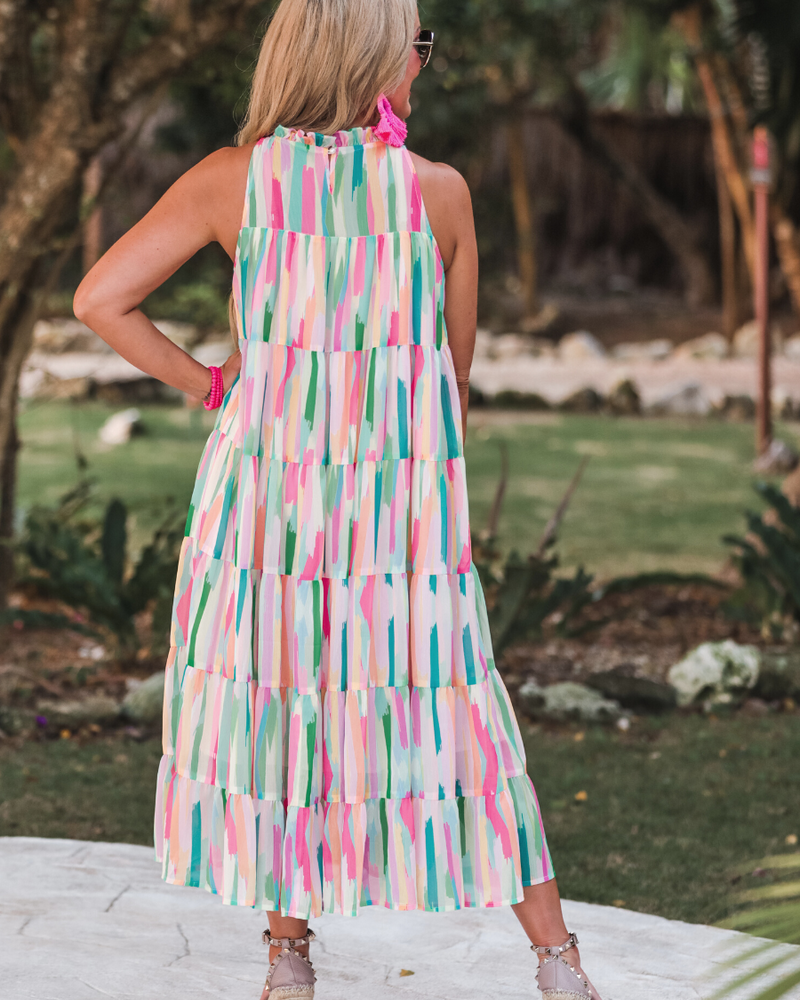 sleeveless dress with a ruffled halter neckline, singular button closure, tiered babydoll style silhouette, and a midi length with lining on a painterly print fabric in multi