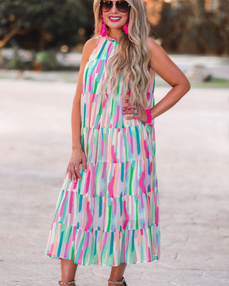 sleeveless dress with a ruffled halter neckline, singular button closure, tiered babydoll style silhouette, and a midi length with lining on a painterly print fabric in multi