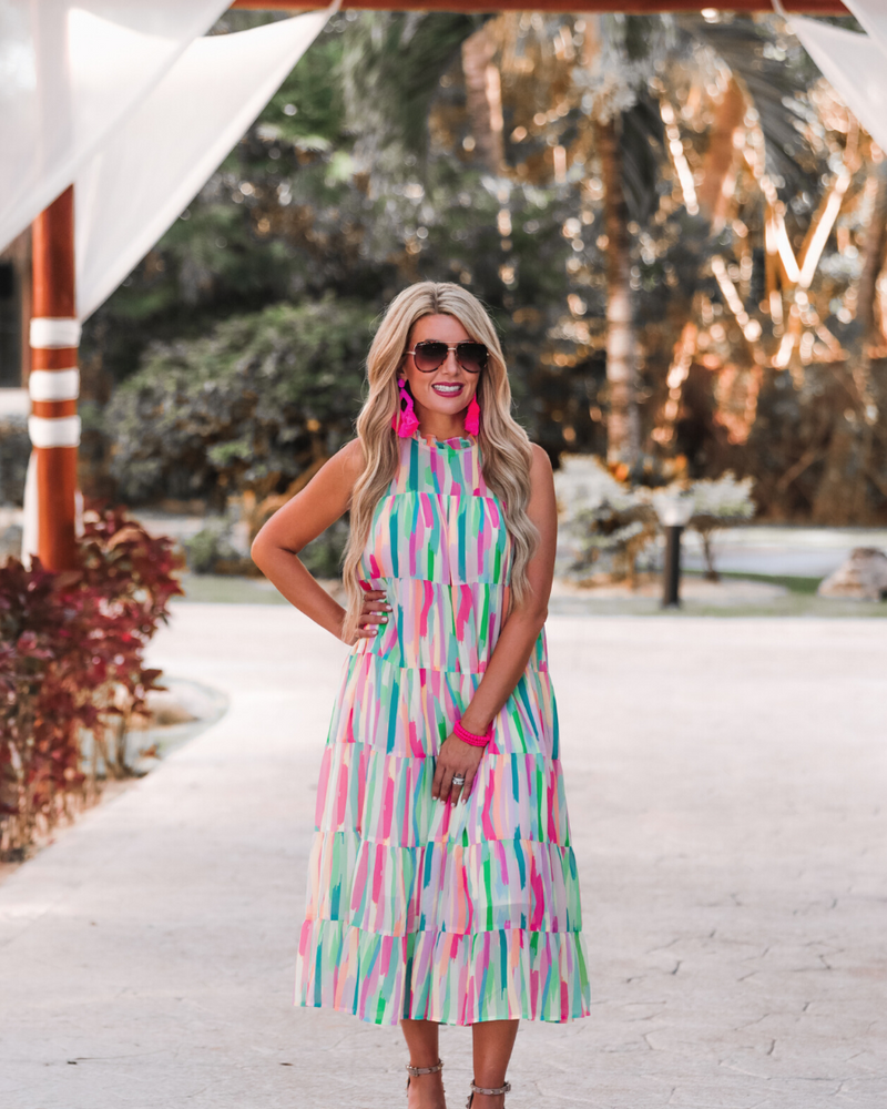 sleeveless dress with a ruffled halter neckline, singular button closure, tiered babydoll style silhouette, and a midi length with lining on a painterly print fabric in multi