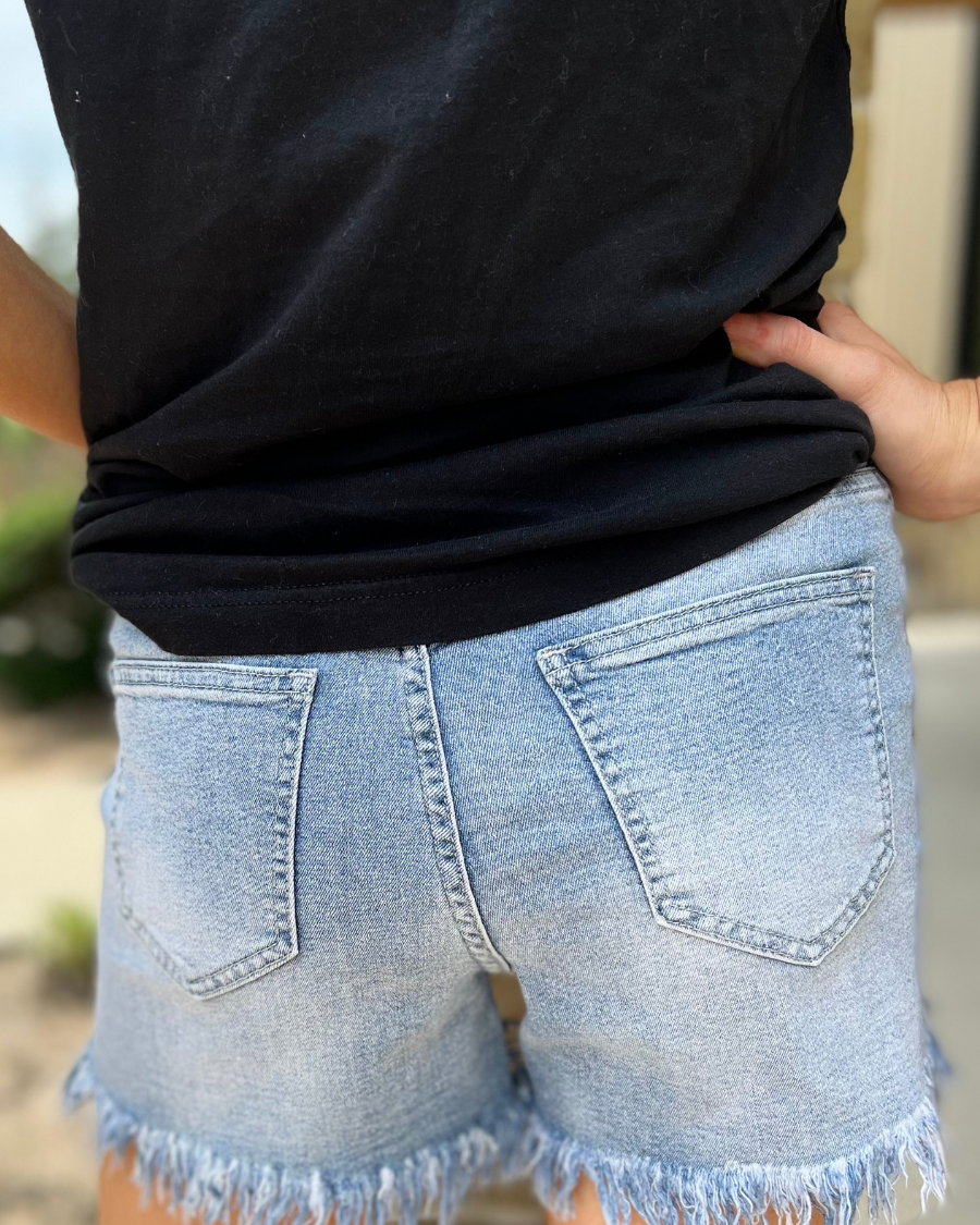 mid-rise denim shorts with rhinestone fringe, a frayed hem, full classic pockets, button zip fly with belt loops, distressed detailing, and a medium wash