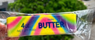 Packaged salted butter bar with colorful tie-dye design held by a hand, blurred greenery in the background.