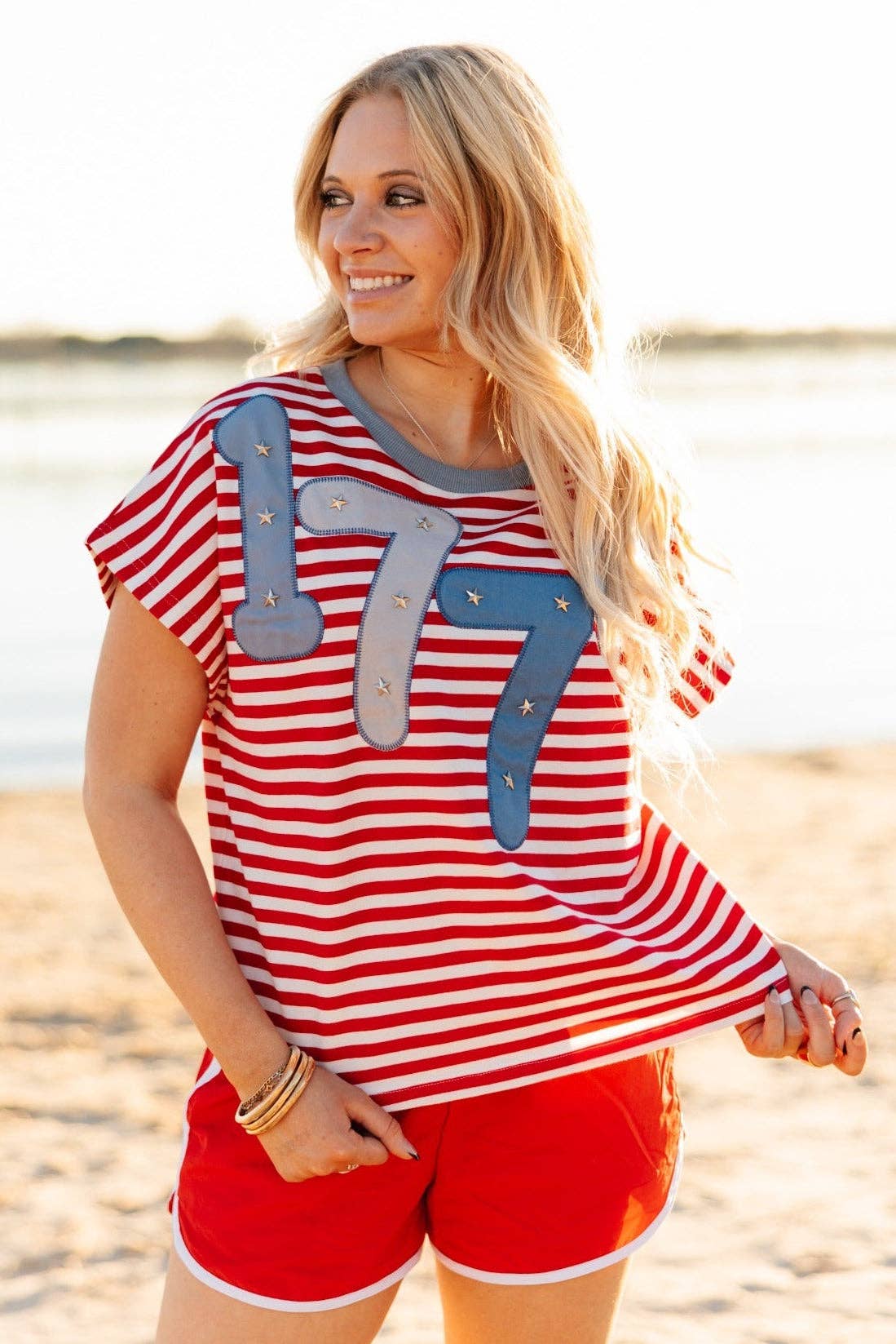 a high-stretch oversized short-sleeve stripe top with a crew neckline, a horizontal stripe pattern (red and white), bold denim 1776 patch detail, tiny star accents, a relaxed easy drape, and unlined