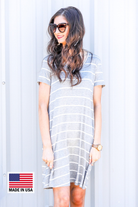 a soft stretchy knit dress with a V-neckline, short sleeves, a relaxed A-line silhouette, a straight hemline, and a horizontal white stripe pattern on a solid heathered grey background with a MADE IN USA watermark in the bottom left hand corner