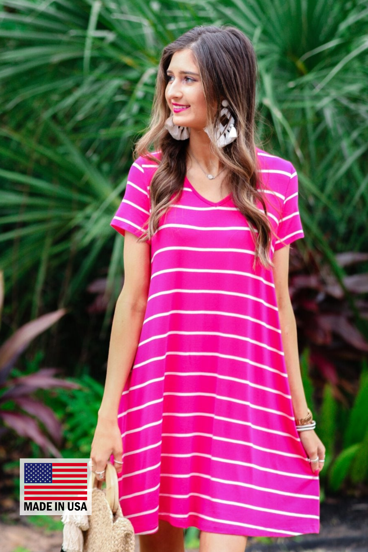 a soft stretchy knit dress with a V-neckline, short sleeves, a relaxed A-line silhouette, a straight hemline, and a horizontal white stripe pattern on a solid hot pink background with a MADE IN USA watermark in the bottom left hand corner