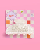 Decorative 'Bride' hair clip on a checkered box against a pink background