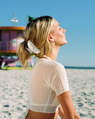 Woman on a beach wearing a white mesh top with a blurred background