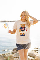 a relaxed-fit beige crew neck tee with a patriotic DTF teddy graphic, short sleeves, standard t-shirt length, unlined construction, and a little stretch that runs large