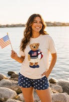 a relaxed-fit beige crew neck tee with a patriotic DTF teddy graphic, short sleeves, standard t-shirt length, unlined construction, and a little stretch that runs large
