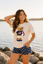 a relaxed-fit beige crew neck tee with a patriotic DTF teddy graphic, short sleeves, standard t-shirt length, unlined construction, and a little stretch that runs large